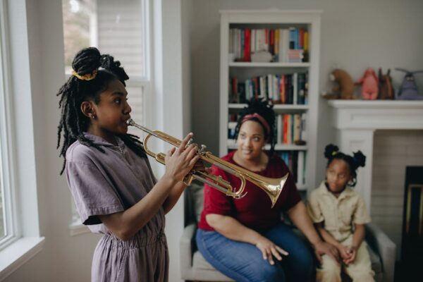 A child plays the trumpet indoors while family observes, creating a warm, musical atmosphere.