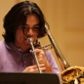 Close-up of a young man playing a trombone indoors, focusing intensely.