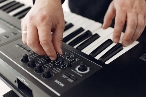 Close-up of hands adjusting synthesizer controls with piano keys in view.