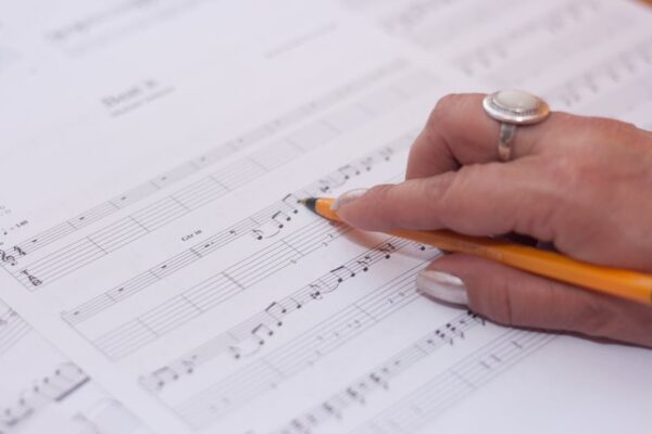 Detailed shot of a hand writing music notes on sheet music, reflecting creativity and composition.