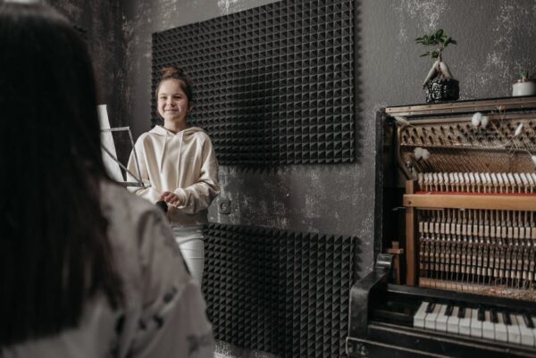 A young girl smiling during a music lesson in a studio with an open piano.