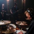 A band playing instruments in a rehearsal studio with drum kit, saxophone, and bass guitar.