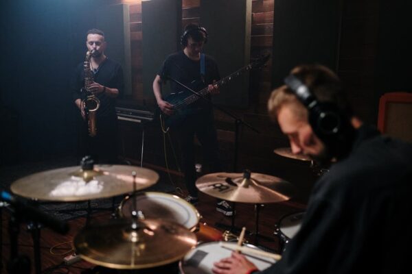 A band playing instruments in a rehearsal studio with drum kit, saxophone, and bass guitar.