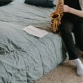 A child sitting on a bed playing a saxophone with music sheets in a cozy bedroom setting.