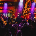 Live band performing in a lively and colorful club atmosphere with a cheering crowd enjoying the music.