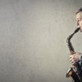 Elderly man passionately plays saxophone against a textured wall. Side profile.