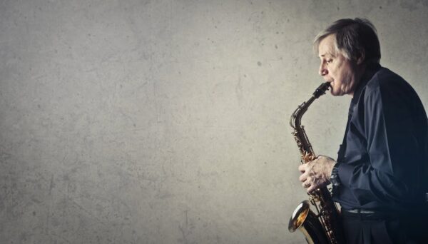 Elderly man passionately plays saxophone against a textured wall. Side profile.