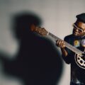 An African American man passionately playing an acoustic guitar, casting a dramatic shadow.