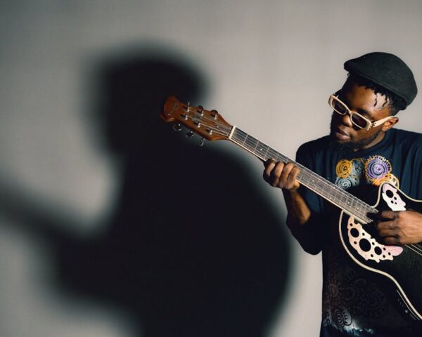 An African American man passionately playing an acoustic guitar, casting a dramatic shadow.