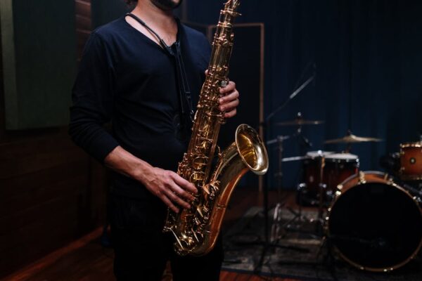 Close-up of a saxophone player in a dimly lit music studio with drums in the background.