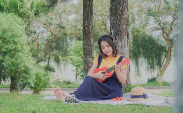 Woman enjoying music outdoors while playing ukulele, surrounded by nature.