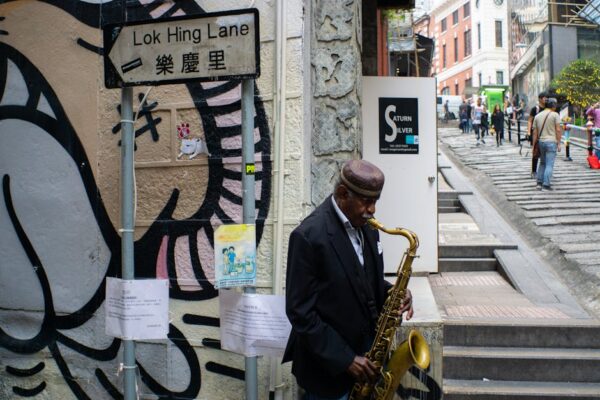 A street musician plays saxophone on Lok Hing Lane, Hong Kong's bustling urban scene.