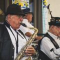 Elderly musicians perform with saxophone and trumpet at an Oktoberfest festival outdoors.