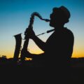 A man playing the saxophone silhouetted against a vibrant sunset sky.