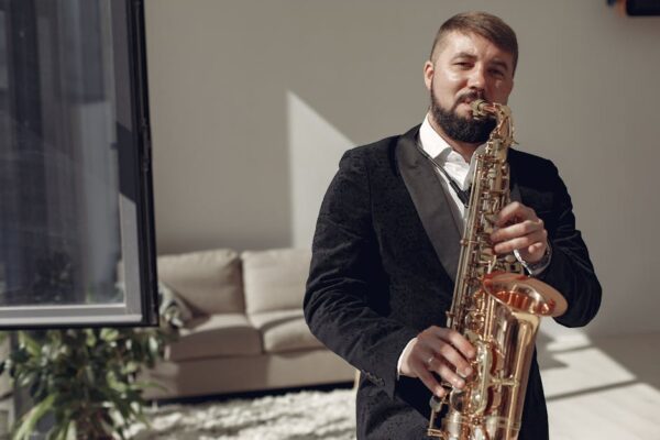 A man in formal attire plays saxophone in a well-lit room, creating a relaxed jazz ambiance.