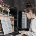 A young girl practicing piano with sheet music in an indoor setting, focused and engaged.