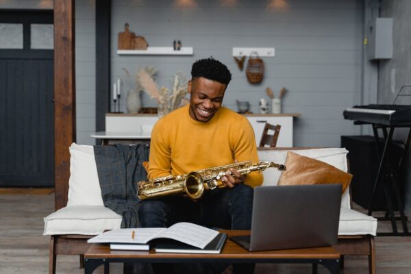 A young man in a yellow sweater plays the saxophone in a cozy home studio setting.