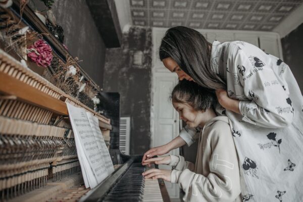 A mother guides her daughter in learning piano amidst a vintage setting, creating a warm educational moment.