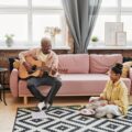 A father and daughter bonding over music in a cozy living room setting.