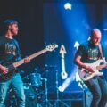 Energetic live performance featuring guitarists on stage with vibrant lighting.