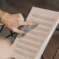 Close-up of a musician pointing at guitar sheet music on a stand indoors.