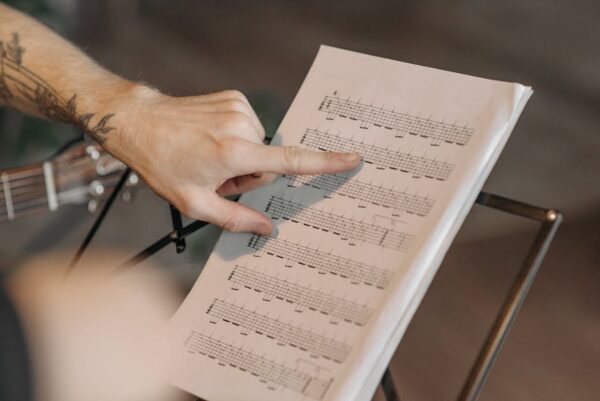 Close-up of a musician pointing at guitar sheet music on a stand indoors.