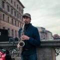 A street musician playing a saxophone on a city bridge, surrounded by urban architecture.