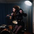 Dynamic female vocalist jumping during a live rock band performance in a soundproof studio.