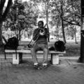 Black and white photo of a street performer playing the trombone on a park bench in Campinas, Brazil.