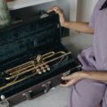 A person holding a trumpet case with a brass trumpet inside, ready for a music session.