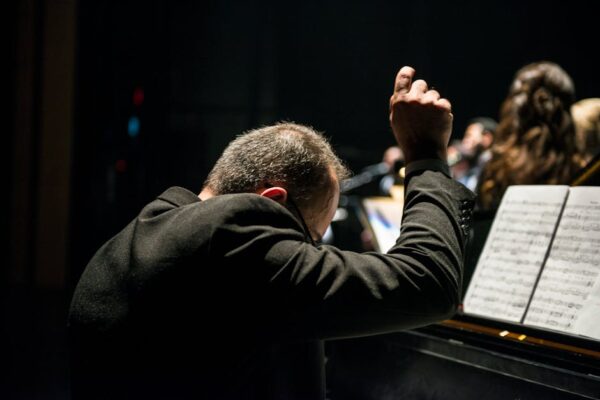A conductor passionately leads an orchestra during a live performance with visible sheet music.