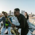A lively band performing on a rooftop during sunset, featuring a saxophonist and lively dancers.