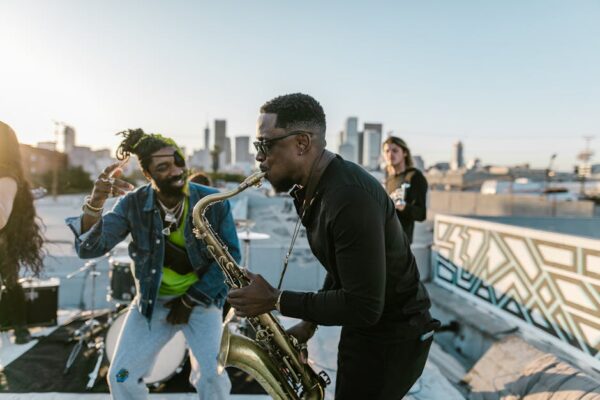 A lively band performing on a rooftop during sunset, featuring a saxophonist and lively dancers.