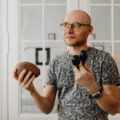 Bald man with eyeglasses holding maracas and coconut shell indoors.