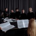 A group of choir members practicing with music sheets in a theater setting.
