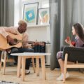 A man teaches a girl guitar in a cozy living room setting during daytime.