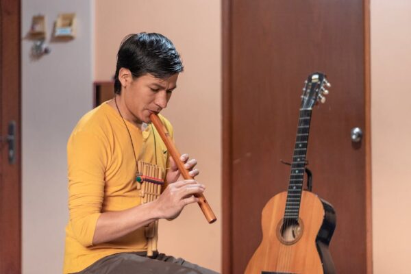 A man playing a wooden flute indoors in Lima, Peru. A guitar is seen nearby.