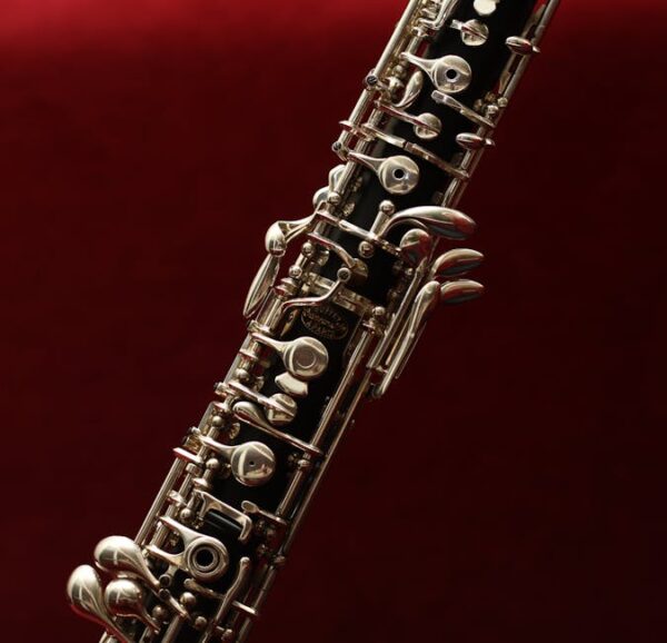 Detailed close-up of an oboe with intricate keys set against a rich red background, highlighting its elegance.