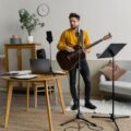 Man playing acoustic guitar during music practice session indoors, with music equipment.