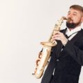Stylish man in a suit playing saxophone with passion against neutral background.