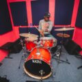 A drummer rehearses on a red drum set in a colorful recording studio in Trinidad and Tobago.