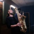 Musician playing saxophone passionately in an indoor recording studio setting.