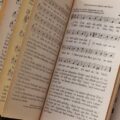 Close-up of an open book displaying musical notes and lyrics on a textured ground surface.