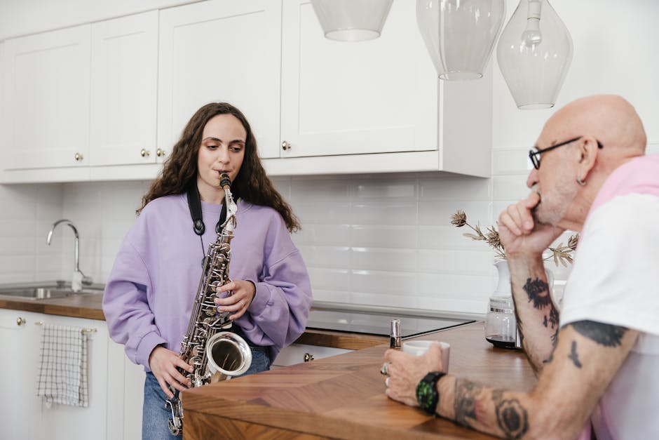 A young woman plays the saxophone while a mentor listens attentively in a modern kitchen setting.