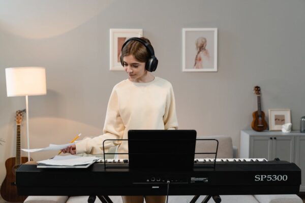 Woman in headphones playing an electronic keyboard indoors, focused on music sheets.