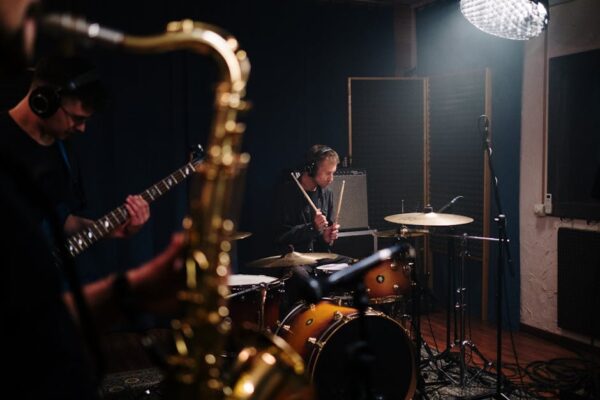 Musicians rehearsing with drums, guitar, and saxophone in a sound studio.