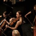 A group of female musicians playing string instruments during an indoor concert.