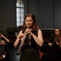 A woman playing the oboe during a classical music concert indoors.