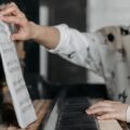 Young girl learning piano indoors, focusing on sheet music and hand placement.