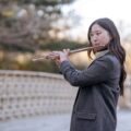 Elegant young woman playing the flute on a peaceful autumn day outdoors.